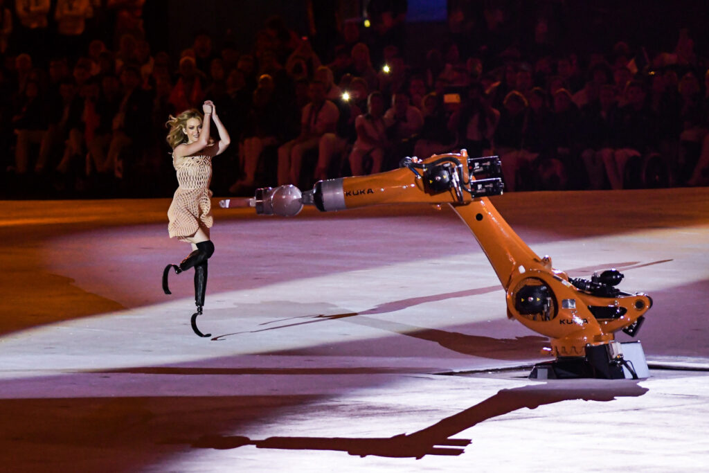 Amy Purdy, destacada figura del movimiento paralímpico, baila en el escenario junto al robot KUKA durante la ceremonia de apertura de los Juegos Paralímpicos de Río 2016, demostrando su destreza con prótesis en las piernas.