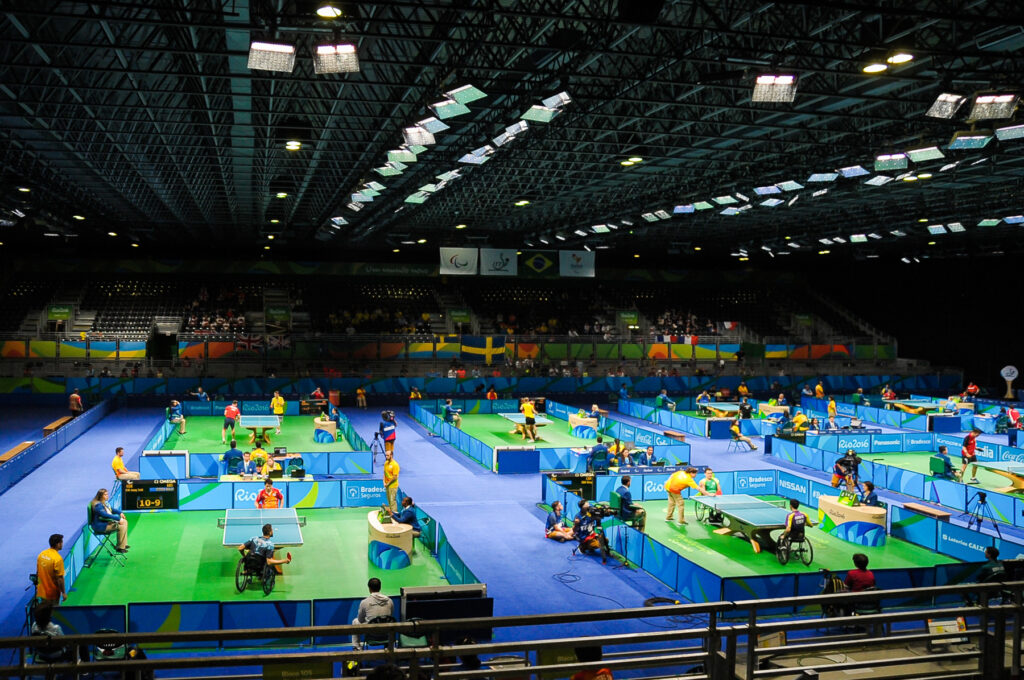 Siete mesas de ping pong distribuidas en el estadio, con partidos en curso al mismo tiempo.