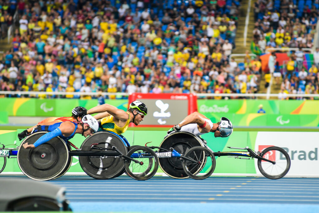 Tres atletas compiten en una carrera de velocidad de 100 metros en silla de ruedas.